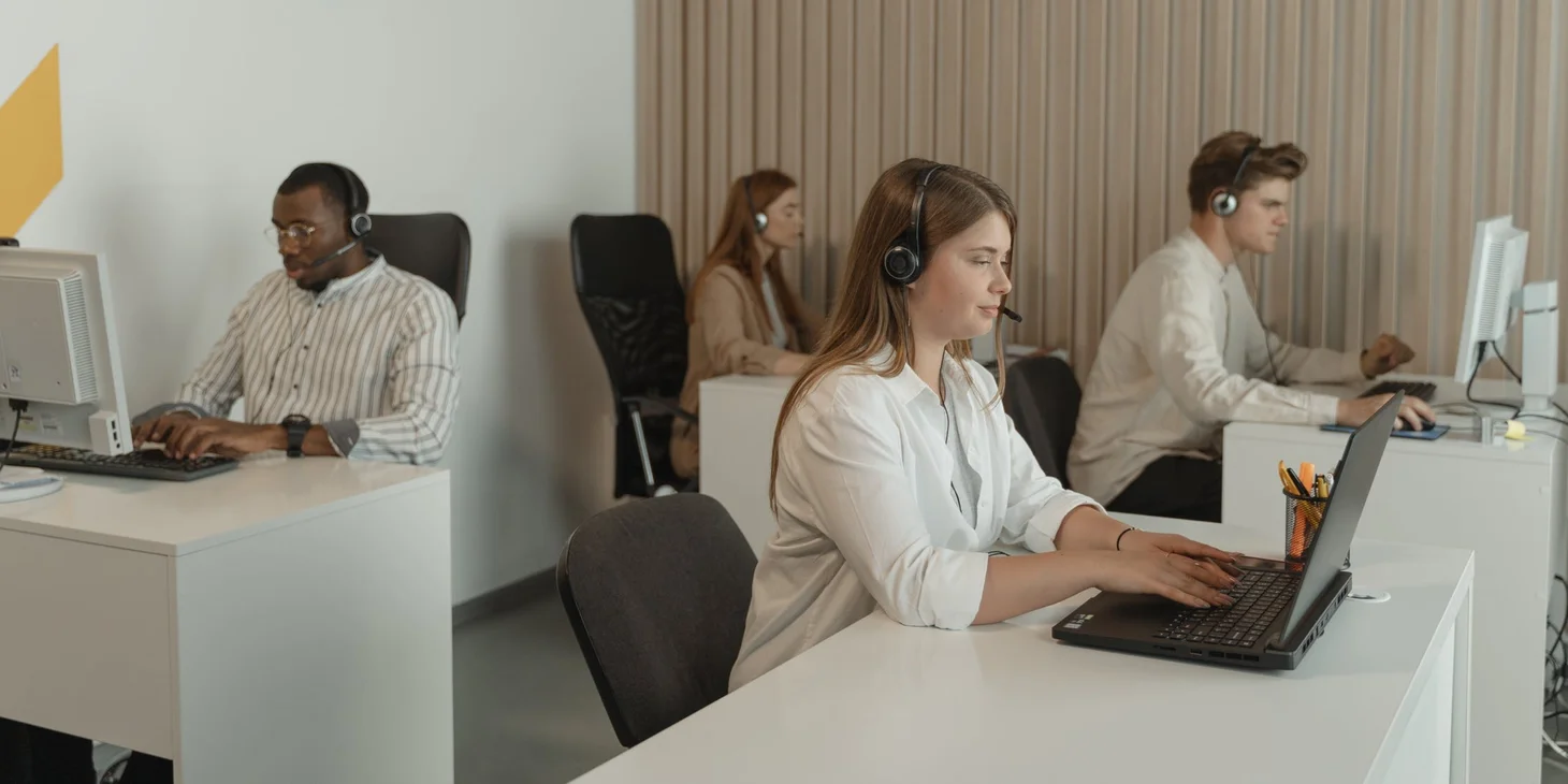 Sales agents with headsets making calls at desks in a bright call center